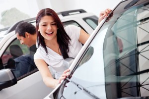 A woman smiling at a vehicle while car shopping in a dealership.